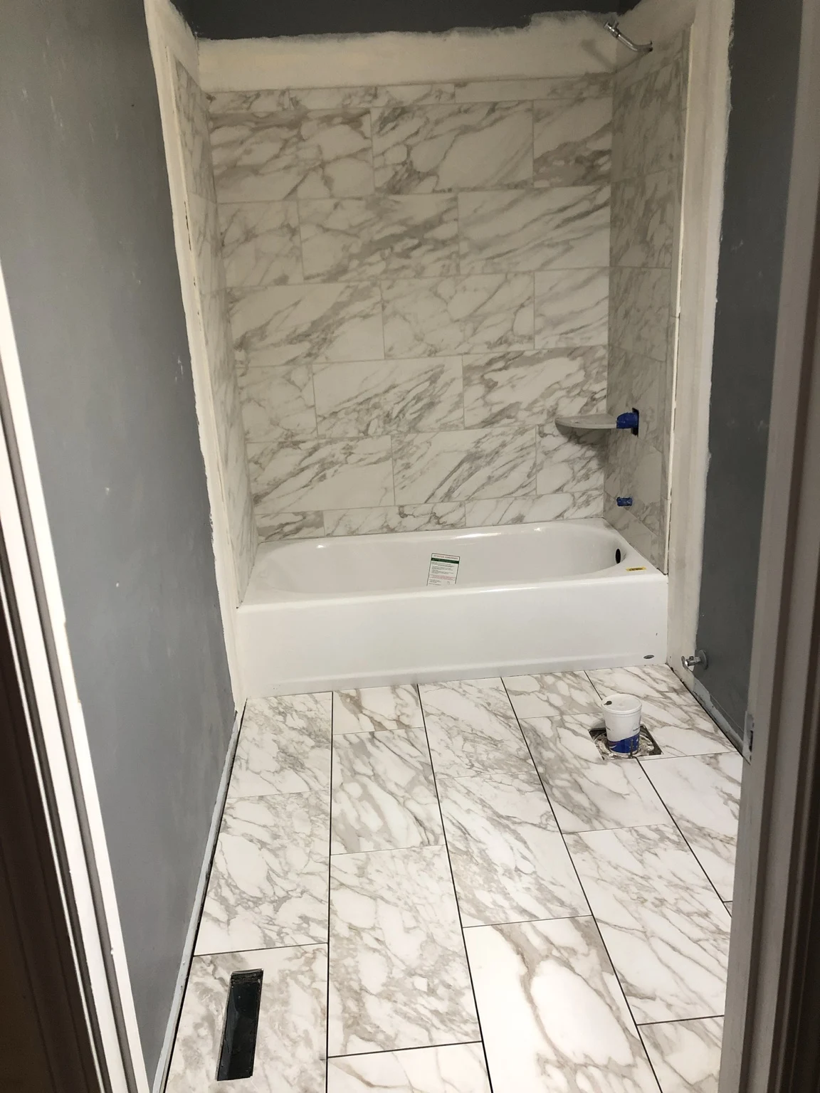 Bathroom renovation in progress with marble-look floor tile and tiled tub walls