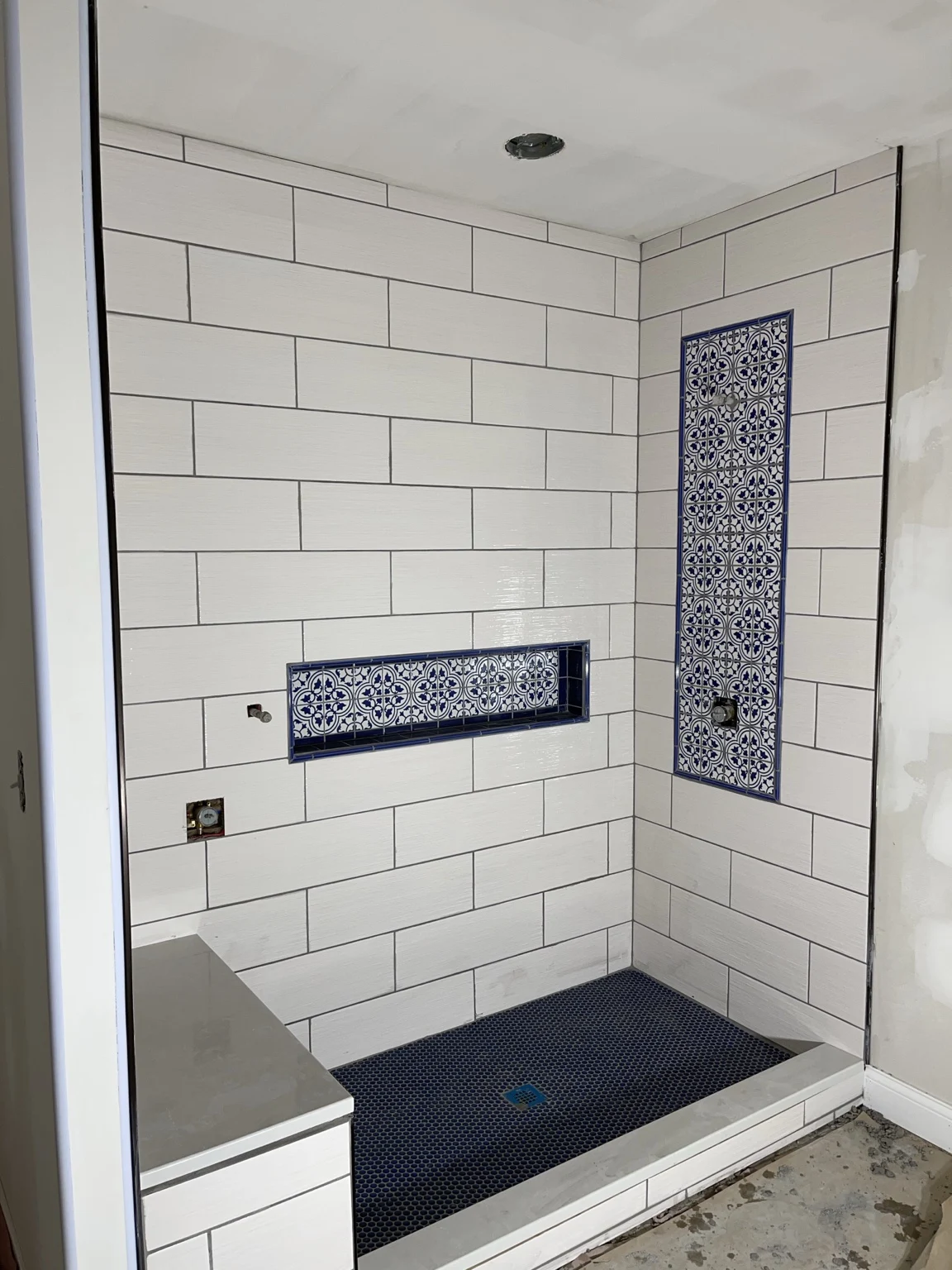 White tiled shower with blue patterned accent tile, a niche, and a bench