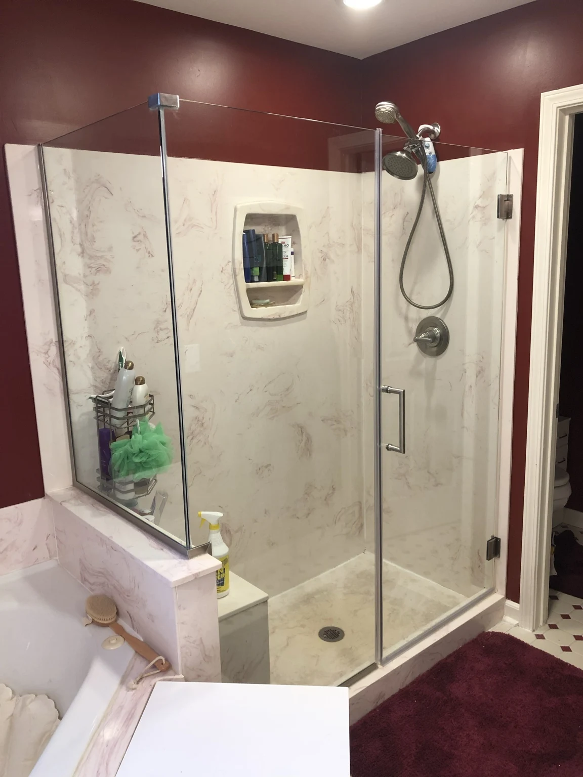Corner glass shower enclosure beside a bathtub in a burgundy-walled bathroom