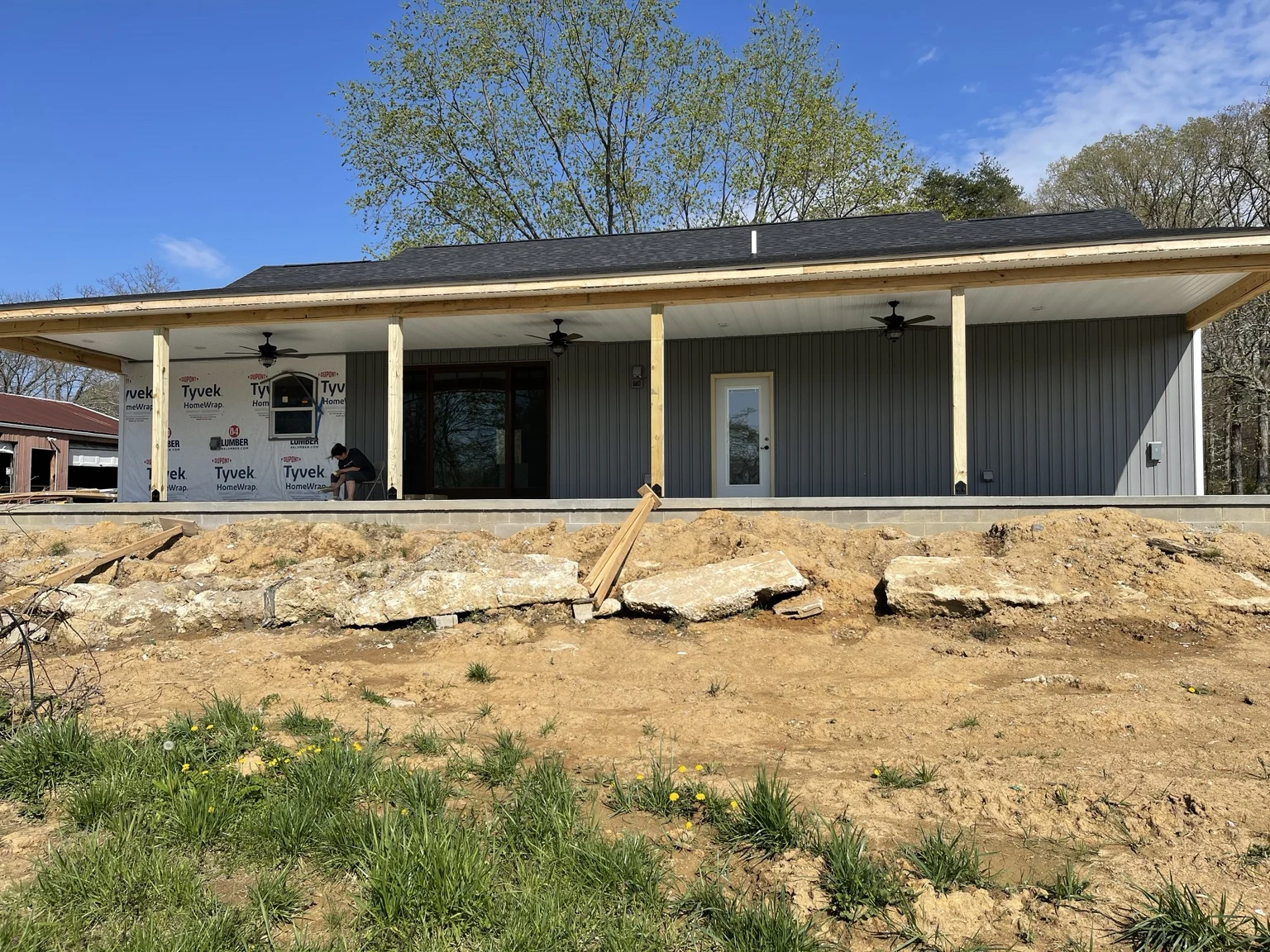 Covered porch under construction with wood posts, ceiling fans, and gray siding