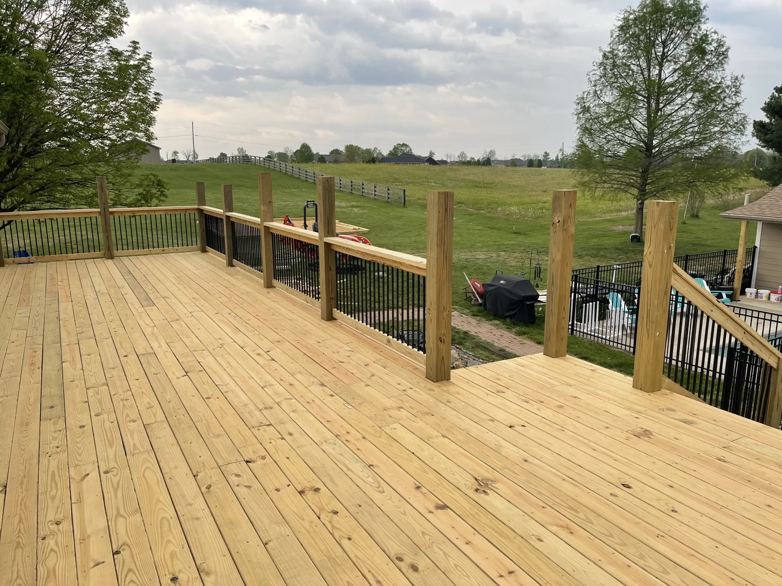 Wood deck with black balusters overlooking a pool and lawn