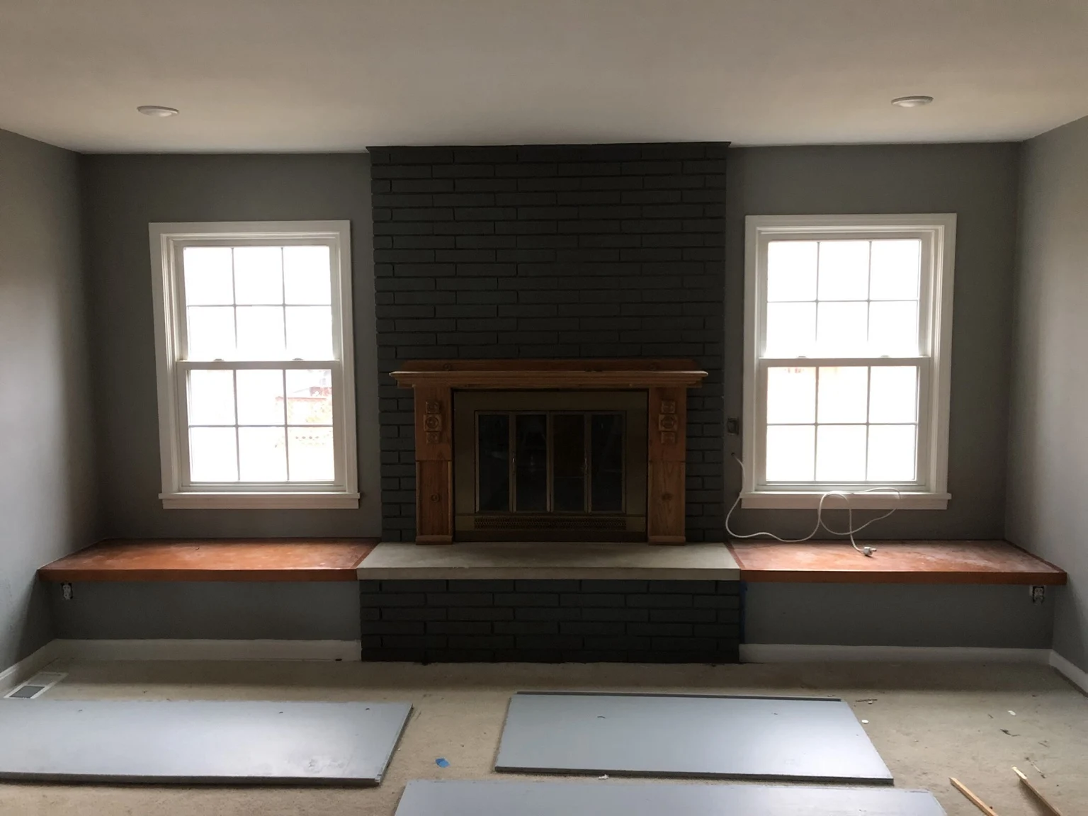 Dark painted brick fireplace with wood mantel and benches beneath two windows