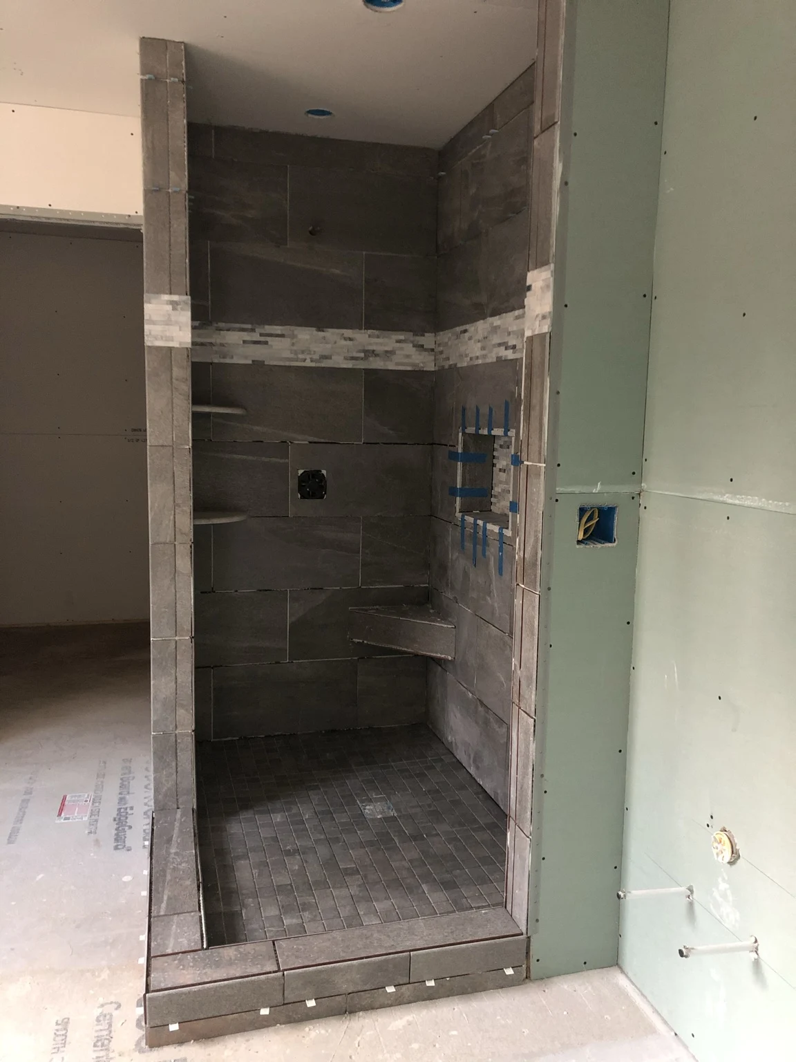 Gray tiled shower with mosaic accent band and niche during installation