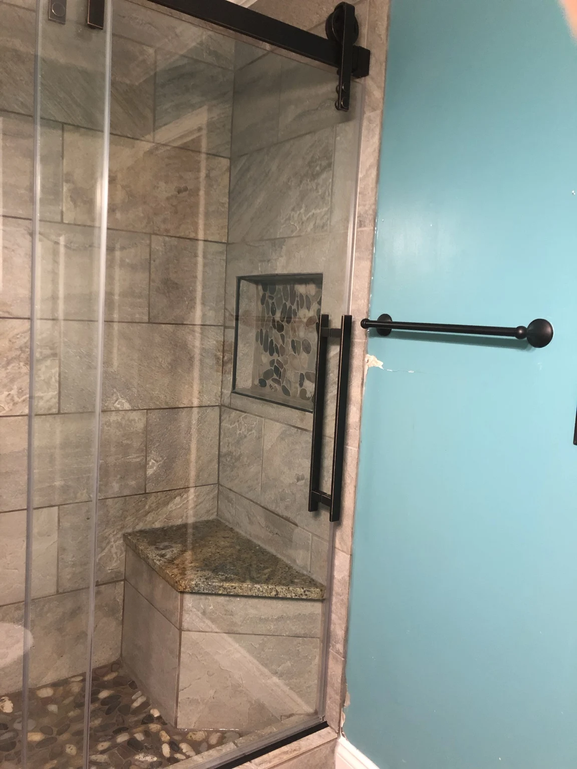 Finished custom tile shower with a granite corner bench, pebble accents, and black sliding glass door