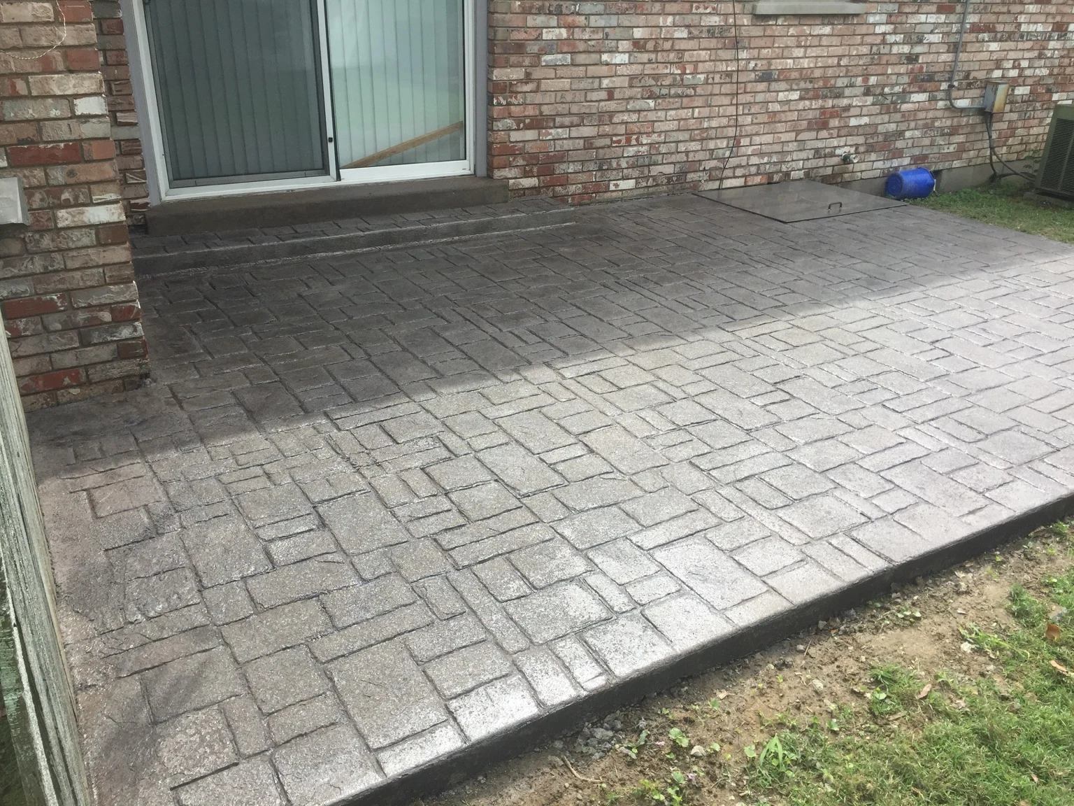 Stamped concrete patio with a stone-pattern surface beside a brick house