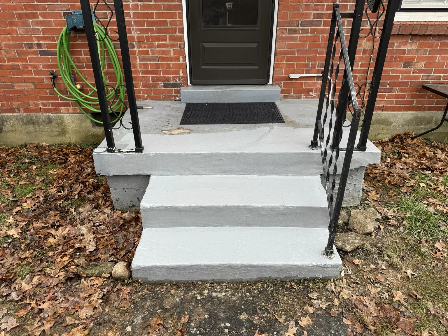 Repaired and coated concrete front steps with existing black metal railings