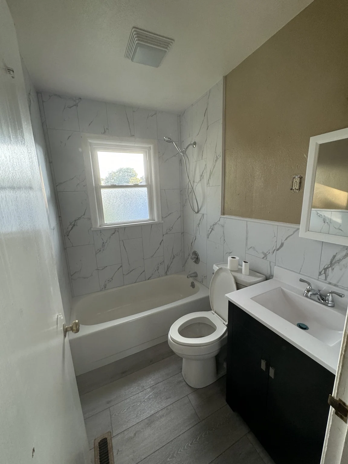 Bathroom project with marble-look tile around a bathtub and a dark vanity